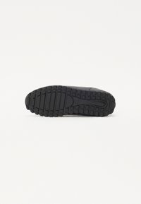 Black athletic shoe sole with textured rubber for traction, featuring a rounded toe and a distinct tread pattern.