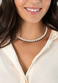 Pearl necklace with white circular pearls of uniform size, resting on a light-colored shirt, with a delicate sheen and smooth texture.