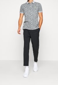 Polo à manches courtes en gris avec un motif abstrait noir, col gris clair contrastant et logo vert. Assorti à un pantalon noir et des baskets blanches.
