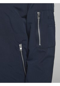 Marinblå ytterkläder med en zip-ficka med silverdetaljer på ärmen, texturerat tyg och förstärkta sömmar.