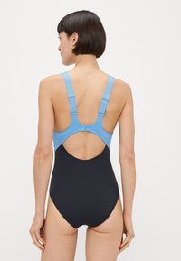 Ολόσωμ ο μαγιό με μπλε επάνω μέρος, μαύρο κάτω μέρος, σχέδιο racerback και ανοιχτή πλάτη με ρυθμιζόμενους ιμάντες. Μαλακή υφή.