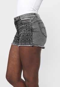 Melnas džinsa šortus ar saplēstu malu, smalku ģeometrisku rakstu sānos un tradicionālo piecu kabatu dizainu.