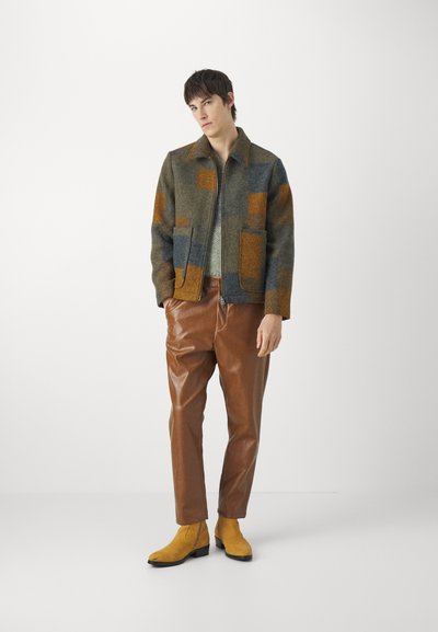 Wool blend jacket with a patchwork design in gray, brown, and orange; features two front pockets. Brown leather trousers and yellow ankle boots.