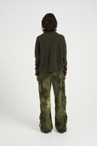 Olive green knitted sweater with a rounded collar, paired with tie-dyed cargo pants featuring multiple pockets and drawstring accents.
