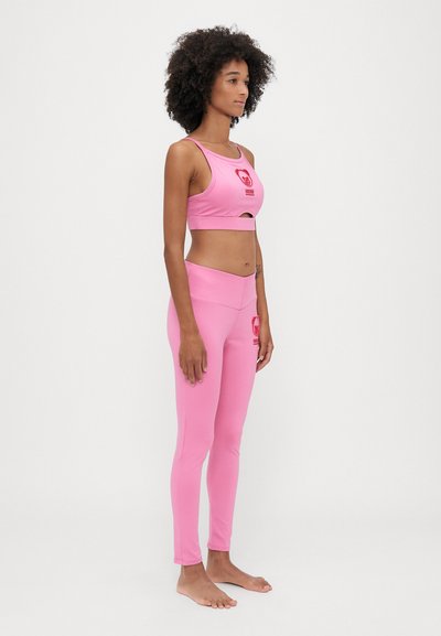 Ružový atletický crop top a legíny vyrobené z elastického materiálu. Top má výkroj a logo medveďa; legíny majú vysoký pás.