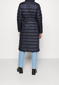 Lång marinblå pufferjacka med horisontell sömnad, åtdragen midja och krage. Bärs över ljusblå jeans och svarta platåstövlar.