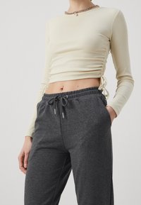 Cream ribbed long-sleeve top with side ruching, paired with loose-fitting dark gray sweatpants featuring an elastic waistband and drawstring.