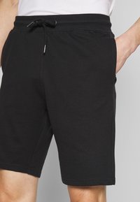 Shorts en coton noirs avec une taille élastique, un détail de cordon de serrage et des poches latérales. Texture lisse, coupe au niveau du genou.