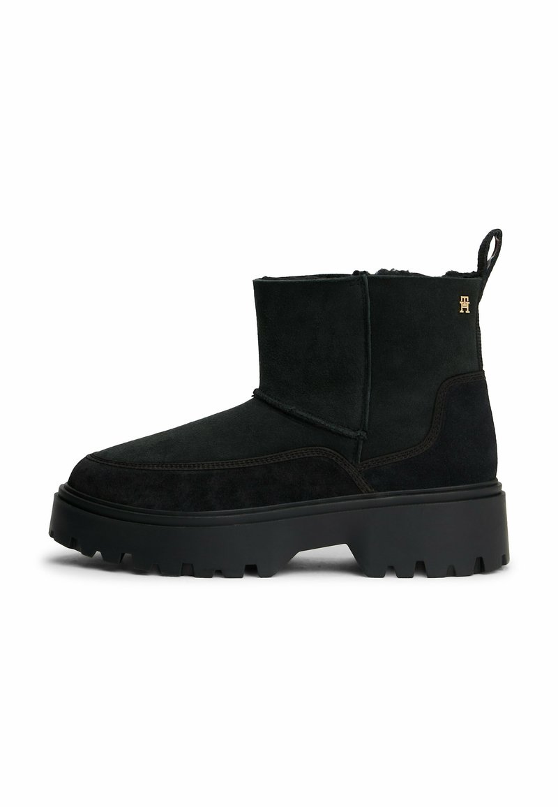 Zwarte suede enkellaarsjes met een ronde neus, dikke rubberen zool en een subtiele logo-accent. Voorzien van een trek标签 voor gemakkelijk aan- en uittrekken.
