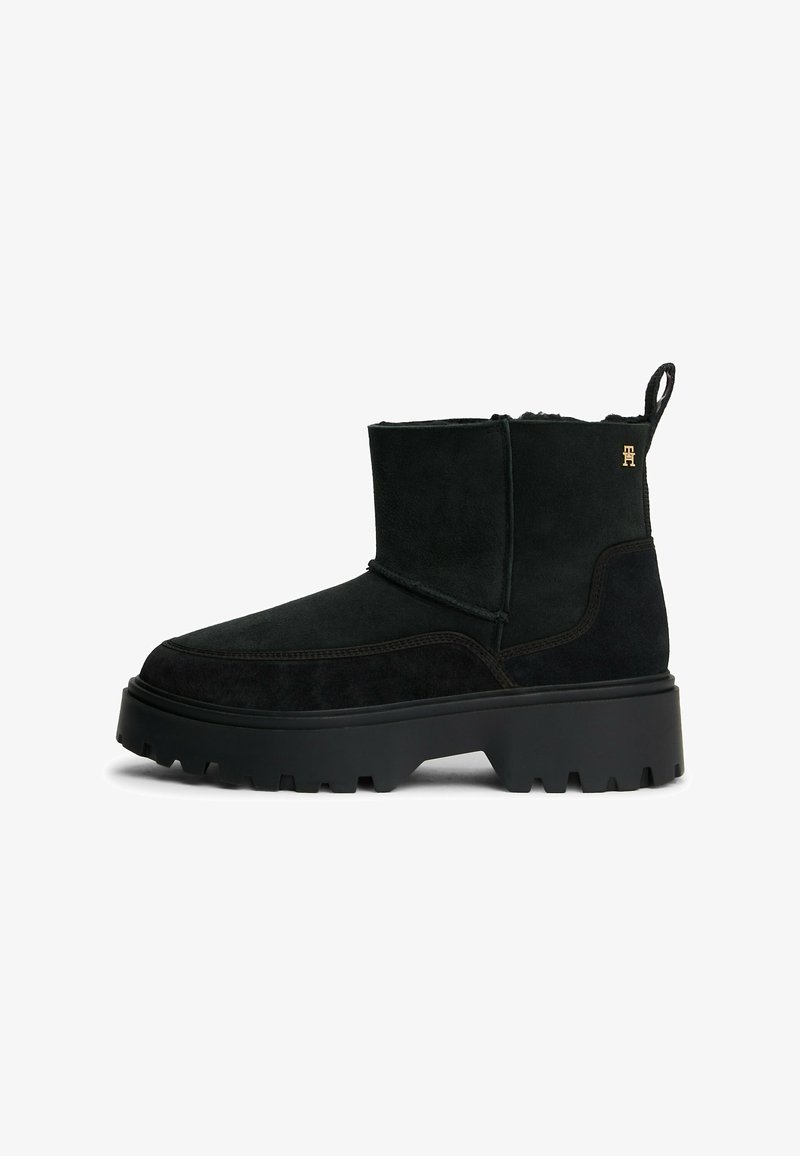 Zwarte suede enkellaarsjes met een ronde neus, dikke rubberen zool en een subtiele logo-accent. Voorzien van een trek标签 voor gemakkelijk aan- en uittrekken.