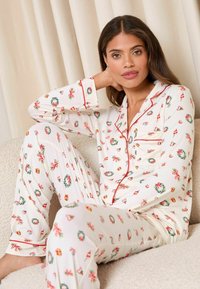 Set de pijamale alb cu motive florale și inimioare, având guler, cusături roșii și un croi relaxat. Material moale cu mâneci lungi și pantaloni.