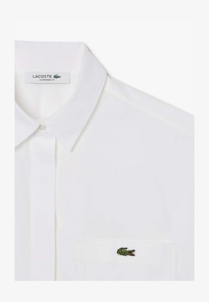 Witte oversized fit shirt met een klassieke kraag, frontale knoopsluiting en een geborduurd groen krokodil logo op de borstzak.