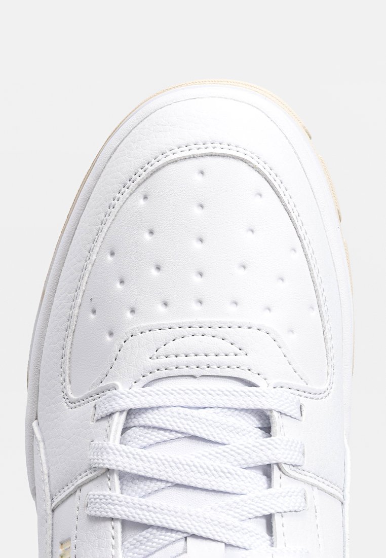 Białe sneakersy z teksturowaną skórzaną cholewką, perforowaną częścią palców, płaskimi białymi sznurowadłami oraz beżową gumową podeszwą.