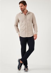 Camisa beige de manga larga con botones, hecha de una tela suave, combinada con pantalones oscuros y zapatillas marinas con acentos grises y cordones.