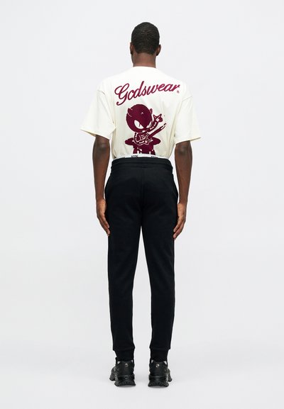 Cream-colored t-shirt with maroon graphic, featuring a character with a guitar. Black pants with elastic waistband and dark shoes.