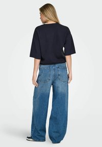 T-shirt oversize bleu marine à manches courtes, associé à un jean bleu clair à jambes larges avec une texture décolorée et des poches arrière.