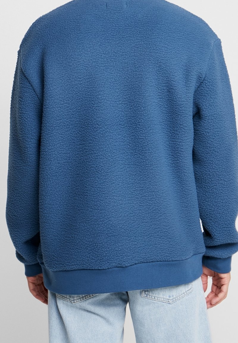 Dunkelblauer Fleece-Sweatshirt mit strukturiertem Oberflächenmaterial, gerippten Bündchen und Saum sowie einem lockeren Schnitt, von hinten gezeigt.