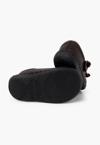 Braune Lederschuhe mit einer schwarzen Gummisohle. Das Design weist runde Akzente und sichtbare Nähte auf, mit einer strukturierten Griffigkeit auf der Sohle.