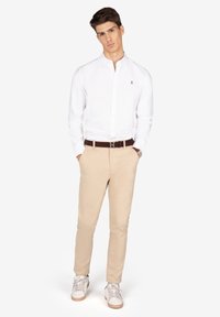 Camisa blanca de botones con un pequeño logo, chinos color beige y zapatillas blancas con detalles marrones. Corte clásico con una textura suave.