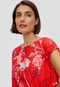 Rood bloemenpatroon jurk met geplooide textuur. Heeft korte mouwen en een ronde halslijn. Accenten zijn gedurfde blauwe en witte bloemen.
