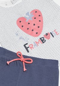 Camisa de manga corta con rayas blancas y azul marino, que presenta un gráfico de un corazón de fresa rosa y el texto "le petit FRAMBOISE"; pantalones de chándal azul marino con cordón coral.
