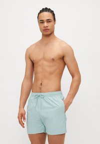 Un short de bain bleu clair en tissu lisse avec une taille élastique et un cordon de serrage. Il est doté de poches latérales et d'une coupe décontractée.