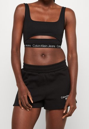 Black cropped top with a square neckline and cut-out design; paired with black shorts featuring a Calvin Klein logo in white.