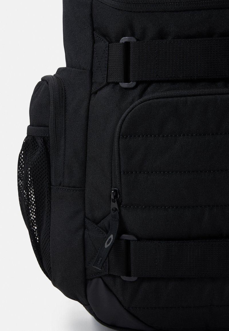 Zaino nero con più scomparti, spallacci regolabili, tasca laterale in rete e accessori resistenti. Tessuto testurizzato con una base liscia.