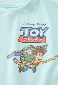 Helles bläuliches Sweatshirt mit einem Grafikdruck der Toy Story Charaktere Woody und Buzz Lightyear in Aktion. Weicher Stoff mit Rundhalsausschnitt.