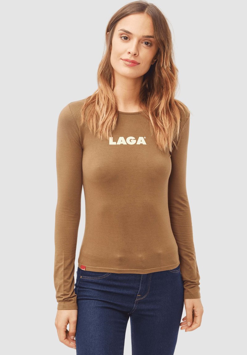 Top marrón de manga larga, hecho de material suave, con un logo blanco de "LAGA" en la zona del pecho y un diseño ajustado. Combinado con jeans oscuros.