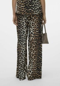 Pantalons à jambes larges en tissu imprimé léopard noir, marron et crème, avec une texture douce et une coupe décontractée. Un petit sac à main gris est porté.