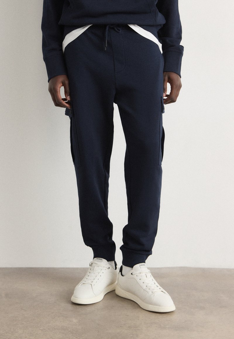 Marineblauwe sweats met zachte stof, voorzien van zijzakken, een elastische tailleband en afgeknipte boorden, in combinatie met witte sneakers.
