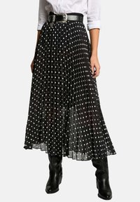 Jupe plissée noire avec des pois blancs, dotée d'une ceinture noire brillante avec une boucle en argent. Portée sur des bottes noires montantes.