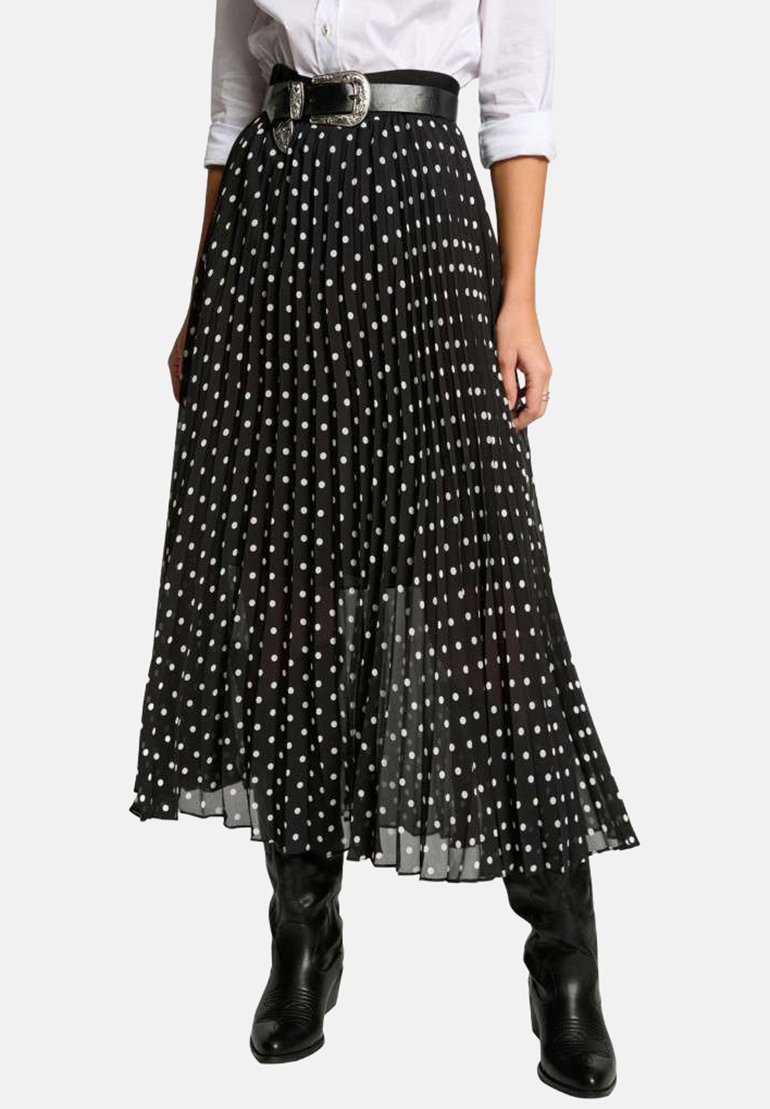 Jupe plissée noire avec des pois blancs, dotée d'une ceinture noire brillante avec une boucle en argent. Portée sur des bottes noires montantes.