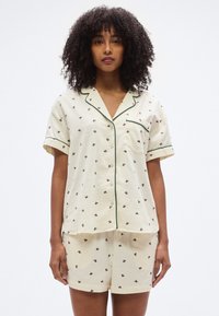 Σετ πυτζάμες κοντομάνικο σε απαλό κίτρινο χρώμα με μικρά λουλουδάτα σχέδια, πράσινη επένδυση και άνετη γραμμή με πουκάμισο με κουμπιά και σορτς.