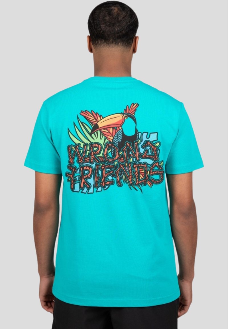 Camiseta de algodón turquesa con un gráfico vibrante de un tucán y follaje tropical. El texto "AMIGOS ERRÓNEOS" se muestra de manera destacada en un estilo decorativo.
