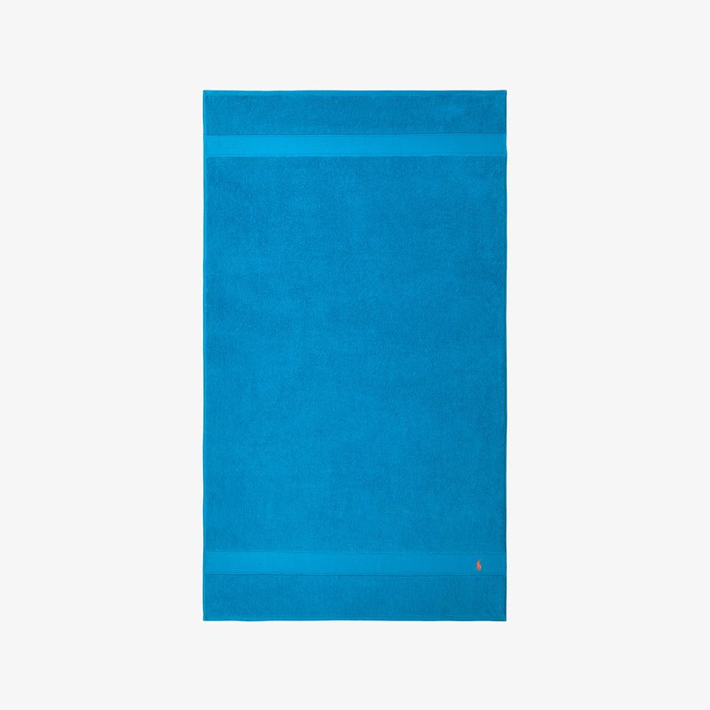 Τουρκουάζ βαμβακερή πετσέτα παραλίας, ορθογώνιο σχήμα, αφράτη υφή, με δύο οριζόντιες ρίγες κοντά στην κορυφή και ένα λογότυπο στη γωνία.
