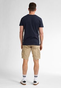 Marineblauwe katoenen t-shirt, beige cargo shorts met zijzakken, witte sokken met zwarte strepen en witte schoenen met bruine zolen.