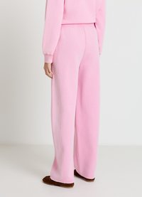 Pantalon de survêtement rose avec une coupe décontractée, une taille élastique et un détail de couture latérale. Fabriqué en matériau doux avec une texture lisse.