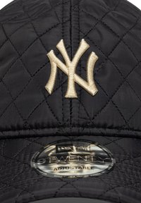 Čierna prešívaná čiapka s vyšitým béžovým logom New York Yankees. Nastaviteľný remienok, hladký povrch a okrúhly šilt s lesklou nálepkou.