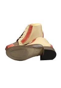 Stivaletti alla caviglia in pelle beige e rossa con punta arrotondata, suole testurizzate e dettagli di cucitura artigianale. Presentano lacci e un tacco basso a blocco.