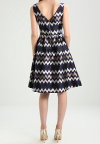 Mörkblå klänning med zigzagmönster i guld och vitt, ärmlös design, V-back, utsvängd kjol och dold dragkedja i ryggen.