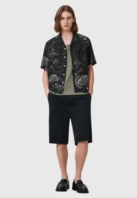 Schwarzes Kurzarmhemd mit weißen Blumenmustern, grünes T-Shirt darunter, schwarze Shorts und schwarze Schuhe. Glatte Textur, lässiges Design.