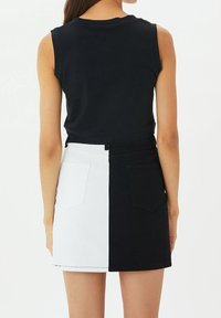 La mini gonna in denim presenta un design a blocchi di colore, divisa in metà nera e metà bianca, con tasche posteriori e vita alta.