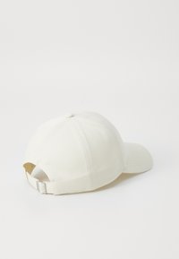 Vit basebollkeps med böjd skärm, tillverkad av texturerat tyg, med en broderad design och en justerbar metallrem baktill.