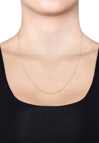 Halskette aus Gold mit gleichmäßig verteilten runden Akzenten, zarten Gliedern und glatter Textur, getragen über einem schwarzen Oberteil.