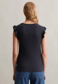 Zwarte ribbel tanktop met ruches aan de mouwen. Gekleed pasvorm, zachte textuur en een ronde halslijn. Gecombineerd met blauwe denim jeans.
