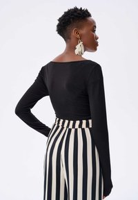 Czarny top z długim rękawem i okrągłym dekoltem z tyłu, w zestawie z czarno-białymi spodniami o wysokim stanie w paski z elastycznym paskiem.
