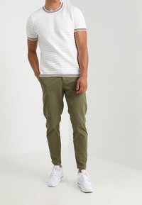 Vit kortärmad skjorta med texturerade ränder och röda accenter, kombinerad med olivgrön taperedbyxor och vita sneakers.