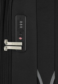 Maleta negra con cerradura de combinación, cremalleras plateadas y tela texturizada. Incluye un logo de la TSA en rojo y elegantes acentos grises.
